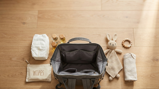 Overhead flat-lay of open gray diaper bag backpack with organized newborn essentials including diapers, wipes, bottles and comfort toys