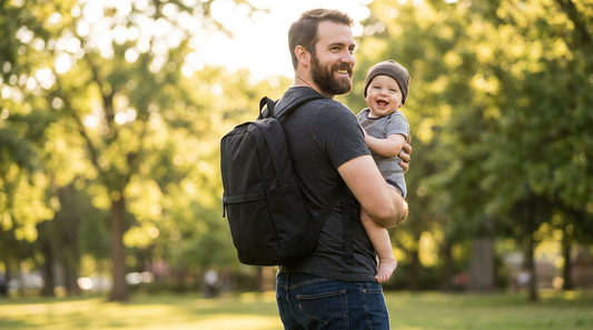 Confident dad wearing a black minimalist Ruvalino diaper bag backpack at the park while holding baby — gender-neutral and stylish