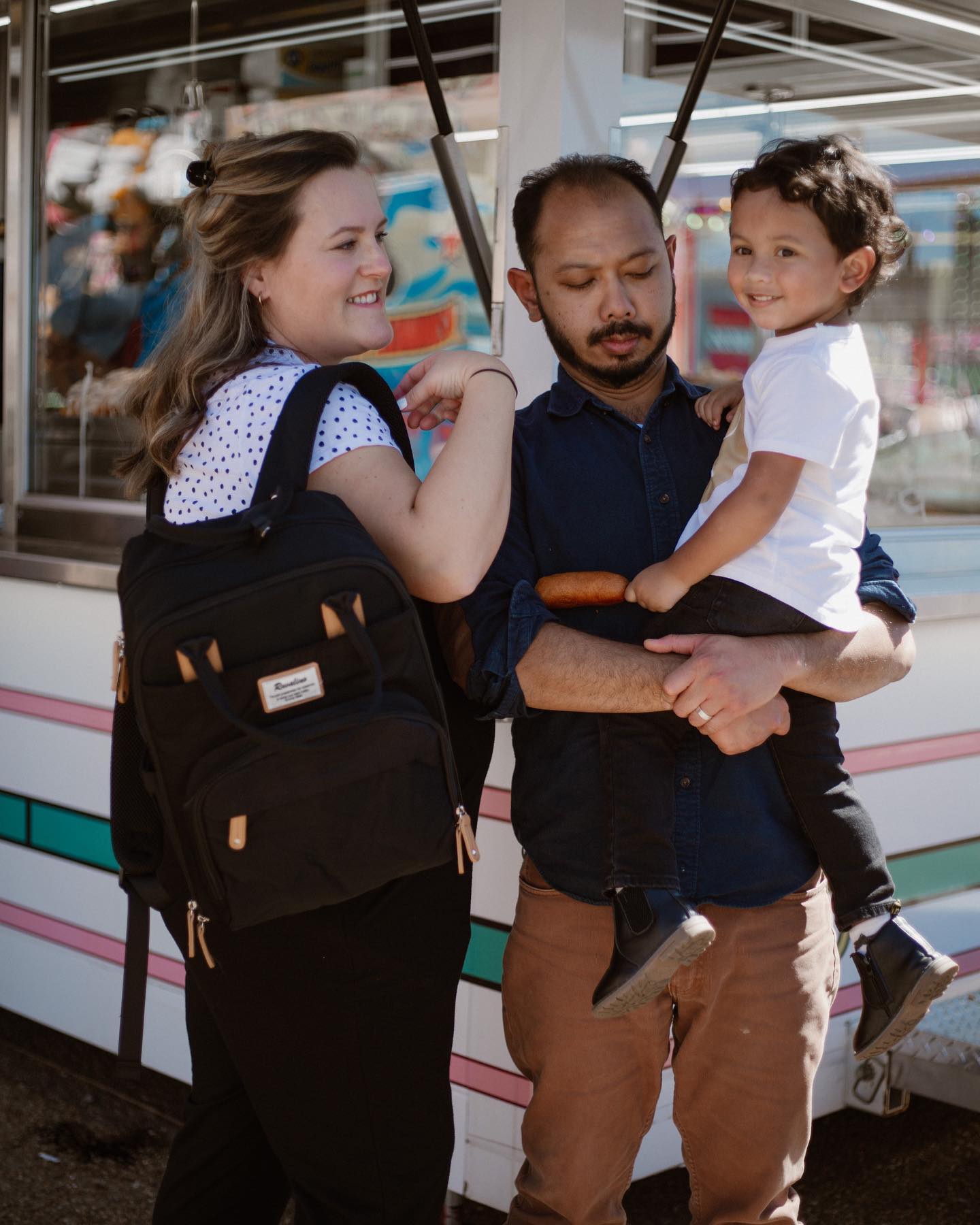 a woman carrying a black backpack smiling at a man holding a toddler in his arms