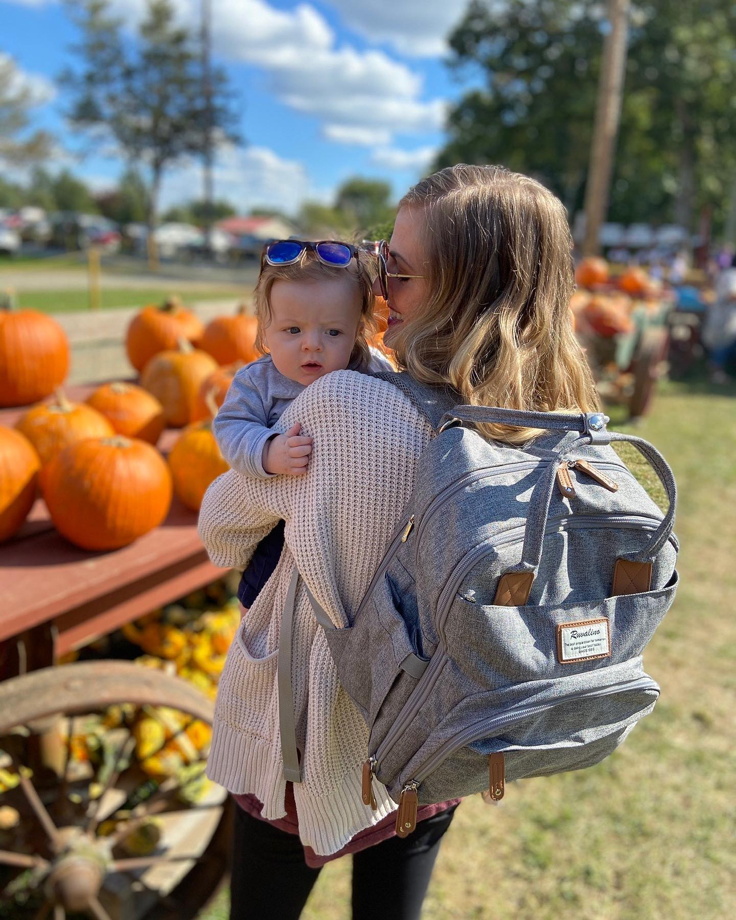 a mom carrying a gray backpack holding a baby 