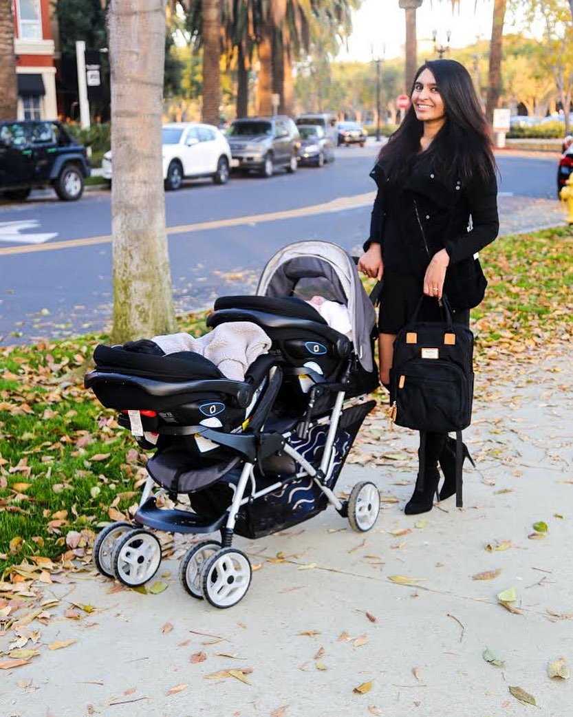 a woman standing behind stroller holding a black backpack